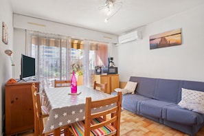 A living room with a sofa, a dining table with chairs, a TV, and a painting on the wall.