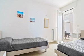 Habitación de hotel con dos camas, puerta corrediza de vidrio a un balcón, una mesita y una silla.