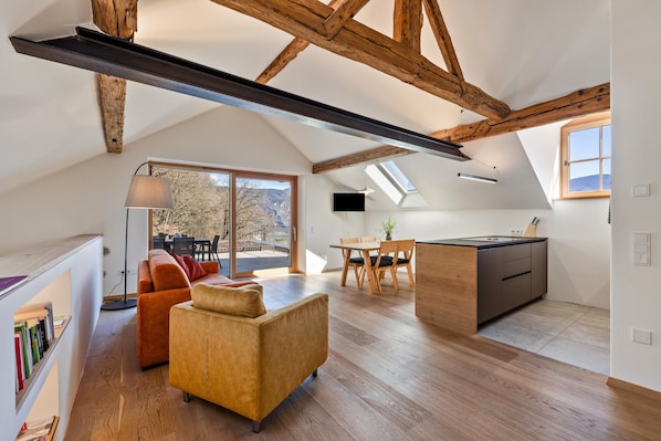 Un loft moderne avec des poutres apparentes, un canapé, un coin repas et une cuisine.