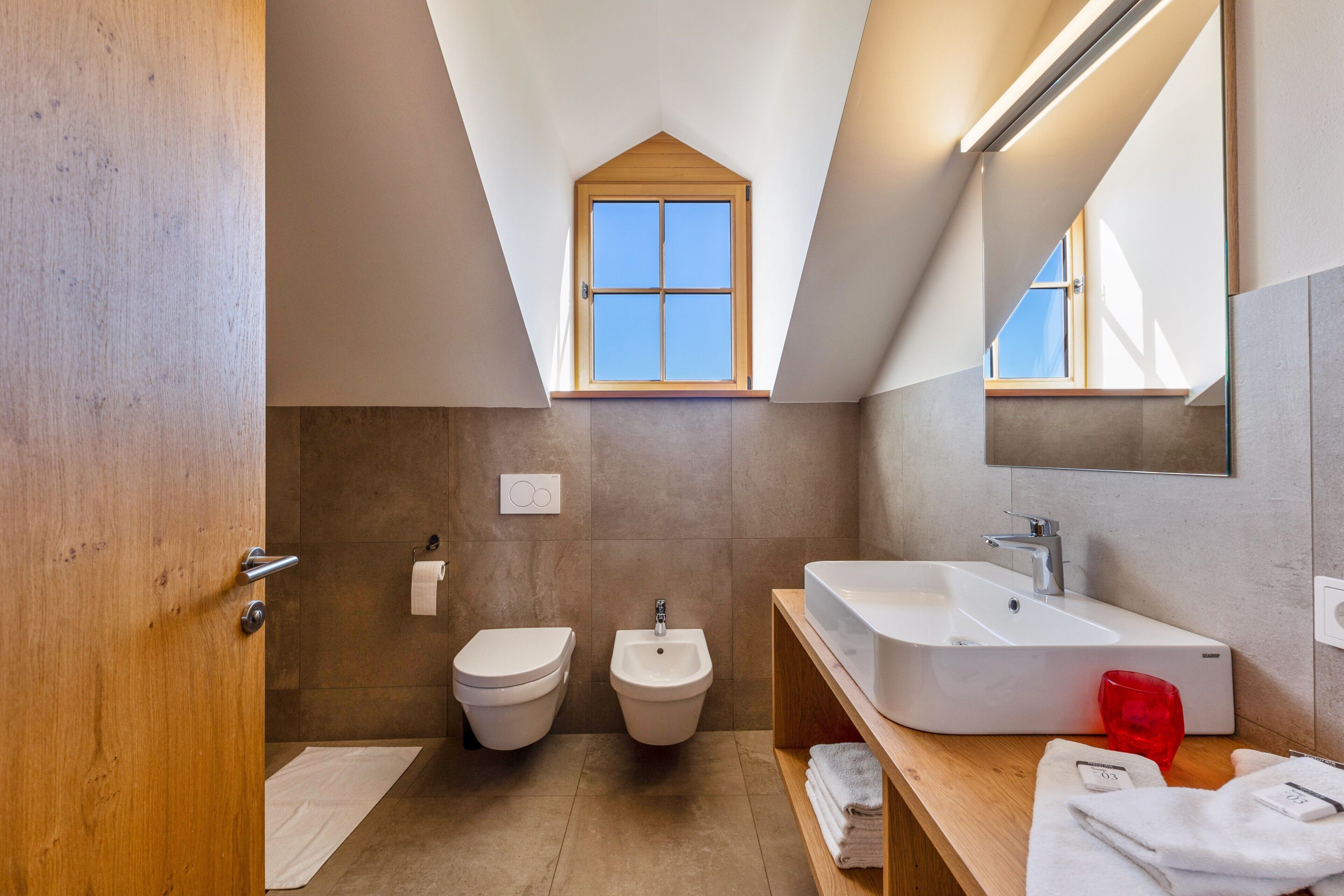 Une salle de bain moderne dotée d’un puits de lumière, d’un bidet, d’un lavabo et d’un miroir.