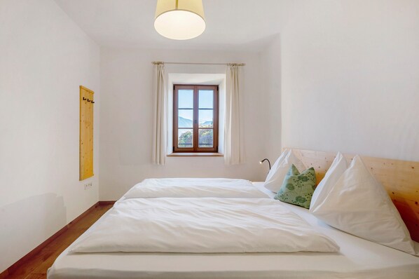 A bedroom with a wooden headboard, a window with curtains, a bed with white bedding, and a wooden floor. - Apartment 'Firmelein 1 Stock' with Mountain View, Private Terrace and Wi-Fi (Missian)