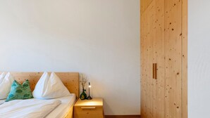 Een slaapkamer met een houten bed, een nachtkastje met een lamp en een houten kledingkast.