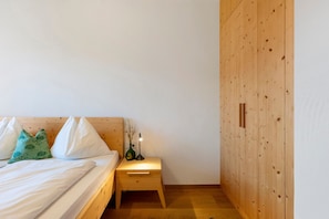 A bedroom with a wooden bed, a nightstand with a lamp, and a wooden wardrobe. - Apartment 'Firmelein 1 Stock' with Mountain View, Private Terrace and Wi-Fi (Missian)