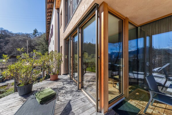 Un bâtiment moderne doté de grandes portes coulissantes en verre, d’une terrasse en bois et de plantes en pot.