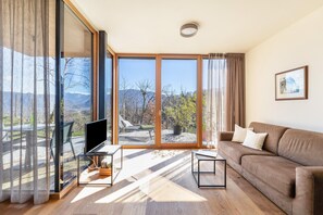 Un salon moderne doté d’une grande porte-fenêtre coulissante donnant sur un balcon, d’un téléviseur à écran plat, d’un canapé marron et d’une table basse.