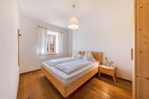 Une chambre à coucher avec un lit en bois, une table de chevet avec une lampe, une fenêtre avec des rideaux et un luminaire suspendu.