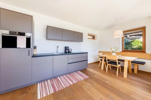 A modern kitchen with grey cabinets, a built-in oven, and a dining area with a wooden table and chairs.