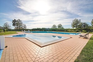 A swimming pool with a tiled deck, surrounded by a grassy area and trees.