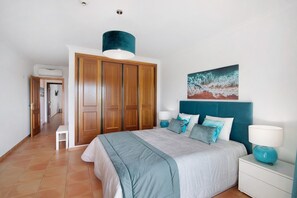 A bedroom with a bed, a nightstand, a lamp, a wardrobe, and a painting on the wall.