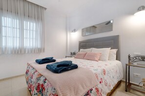 Une chambre à coucher avec un lit, une table de chevet, un miroir et une fenêtre avec des rideaux.