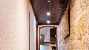 A narrow hallway with wooden flooring, a stone wall on one side, and a kitchen visible through an archway. - Holiday Home 'Dellarose Max' with Private Terrace, Wi-Fi and Air Conditioning (Porto)