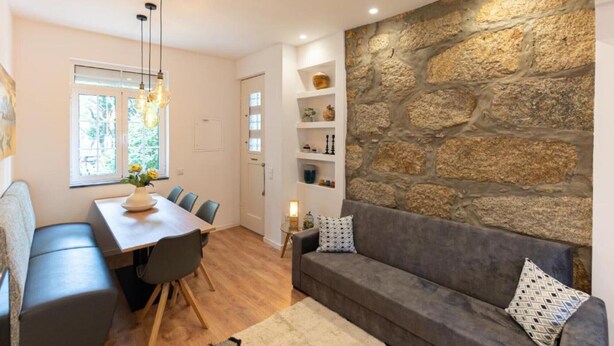 A modern living room with a stone wall, a dining area with a table and chairs, and a sofa with cushions. - Holiday Home 'Dellarose Max' with Private Terrace, Wi-Fi and Air Conditioning (Porto)