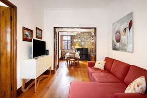 Uma sala de estar com um sofá vermelho, um móvel branco para entretenimento e um quadro na parede.