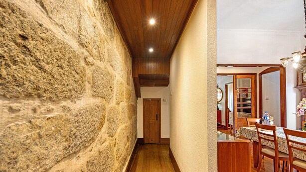 Un pasillo con pared de piedra, suelo de madera y un área de comedor con una mesa y sillas.