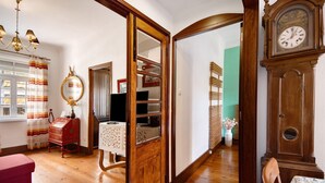 Una habitación con piso de madera, una silla roja, un armario de madera, un espejo y un reloj.