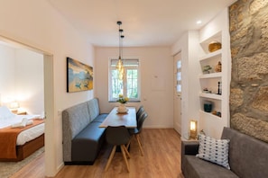 Un espace de vie compact comprenant un lit, un banc, une table à manger avec des chaises, un canapé et un mur décoratif en pierre.