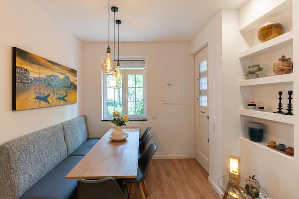Un espace repas comprenant une table en bois, des bancs, des luminaires suspendus, une fenêtre offrant une vue agréable et une étagère décorative.