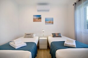 A hotel room with two beds, a nightstand, an air conditioner, and two wall-mounted pictures. - Baleal Atlantic Villa (Ferrel)