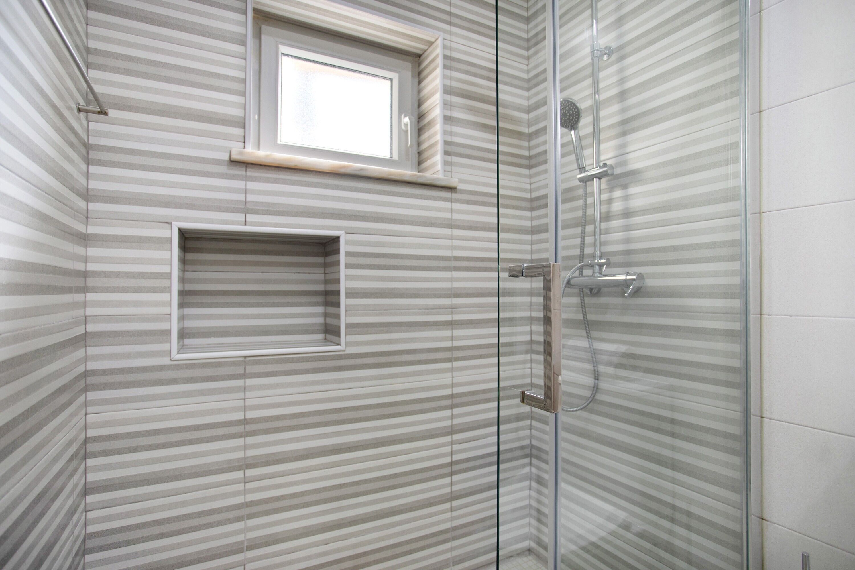 A shower with a glass door, a window above it, and a towel rack.