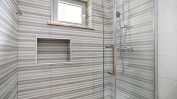 A shower with a glass door, a window above it, and a towel rack.