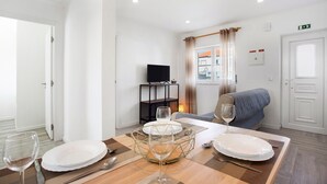 Un comedor con una mesa preparada para dos personas, un televisor sobre un mueble bajo y un sofá al fondo.