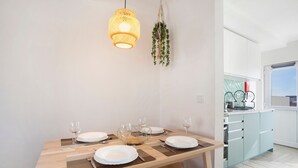 Una mesa de comedor con platos, vasos y cubiertos, una lámpara colgante y una cocina con armarios y una ventana.