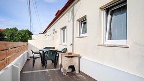 Un balcon avec une table et des chaises, un petit tabouret et une fenêtre avec un rideau.
