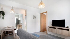 Un salon moderne avec un canapé, une table à manger, un téléviseur et des luminaires suspendus.
