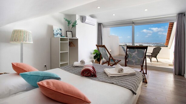 Ein Hotelzimmer mit Bett, Schreibtisch, Stuhl, einem Balkon mit Blick und einem weißen Kleiderschrank.