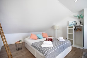 Un dormitorio con cama, almohadas, una mesita de noche, una lámpara, un armario y una planta.