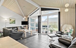 Uma sala de estar moderna com uma janela ampla, sofás de couro, uma TV de tela plana e teto de madeira.
