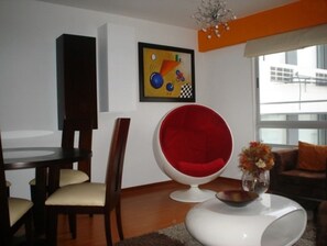 Relax in this stylish living room with a dining area, coffee table, and vibrant chair, surrounded by a beautiful view.