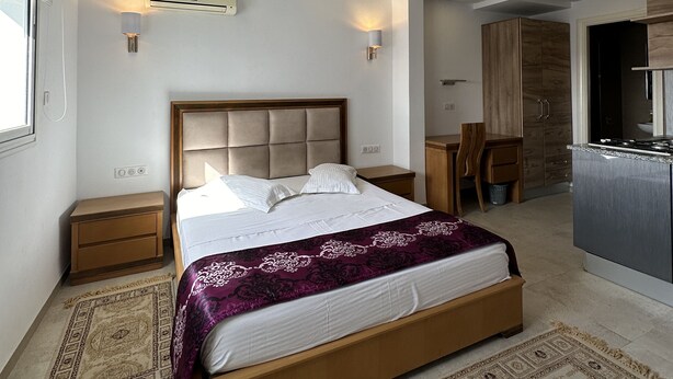 A modern hotel room with a large bed, a wooden nightstand, a desk, and a kitchenette. - Immeuble Gazbar (Gabes)