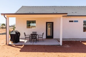 Une maison de plain-pied avec un patio couvert, un barbecue et une porte.