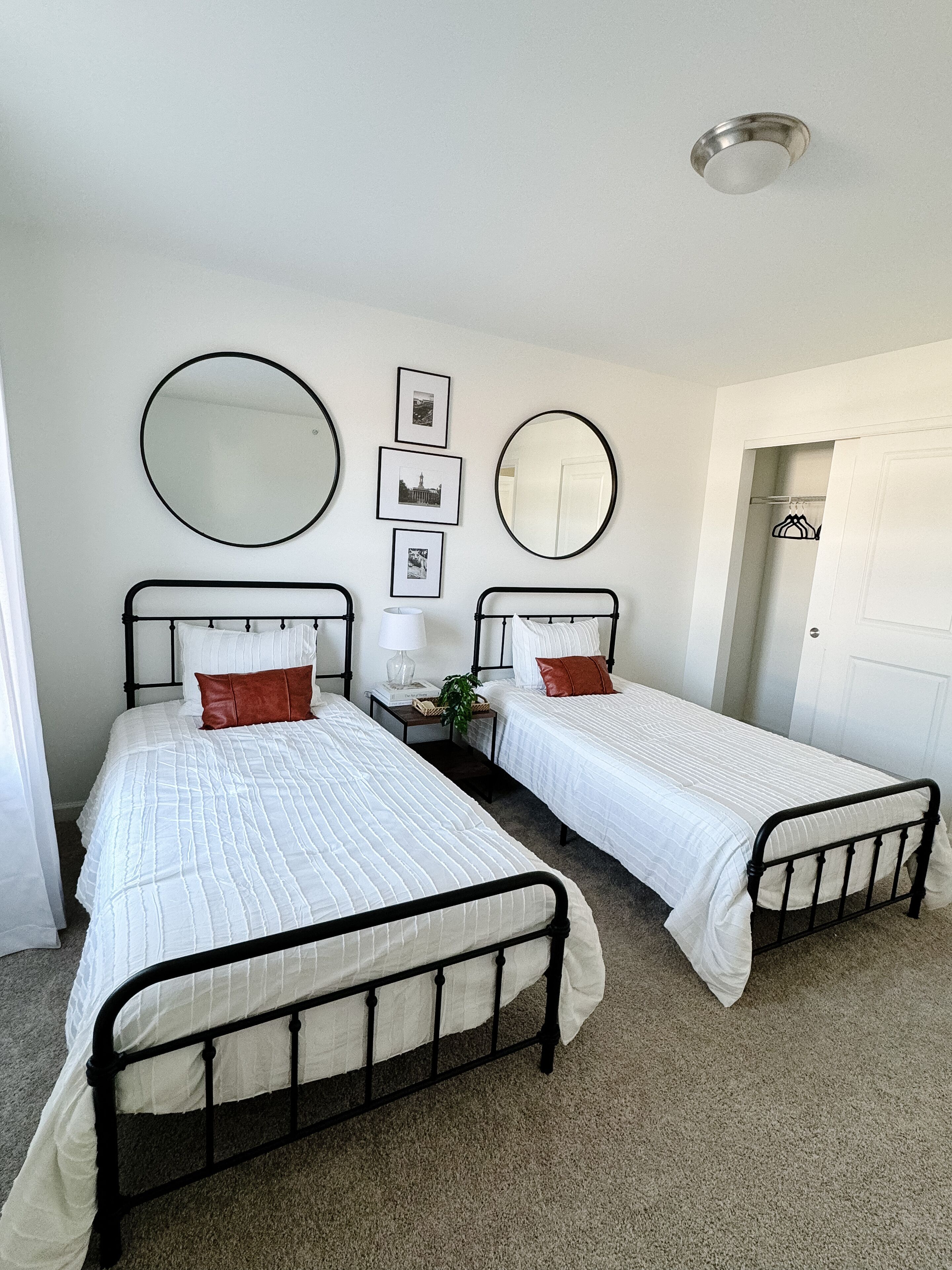 Une chambre avec deux lits simples, un miroir rond et une petite table avec une lampe.