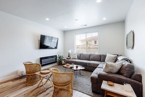A modern living room with a sofa, chairs, a TV, and a window.