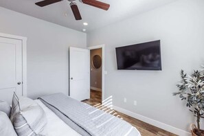 A bedroom with a bed, a ceiling fan, a television on the wall, and a potted plant.