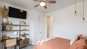A bedroom with a bed, a desk, a chair, a TV, and a ceiling fan.