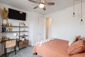 A bedroom with a bed, a desk, a chair, a TV, and a ceiling fan.