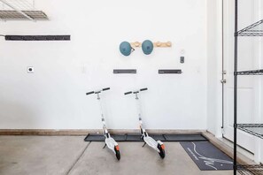 A room with two scooters, a wall-mounted shelf, and a door with a metal rack. - Desert Sky | Experience Adventure & Comfort (Washington)