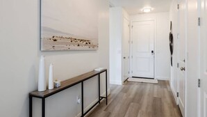 A hallway with a wooden console table, a white door, and a wall-mounted artwork.