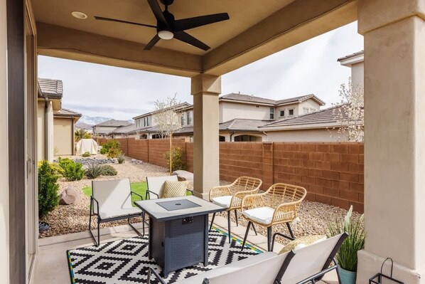 A covered patio with a ceiling fan, outdoor seating, and a view of neighboring houses.