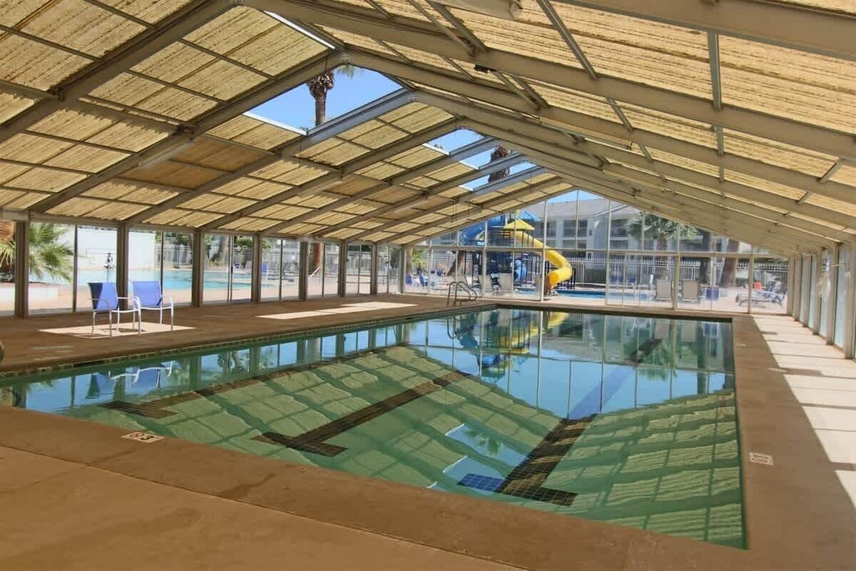 An indoor swimming pool with a glass enclosure, a covered roof, and a slide in the background.
