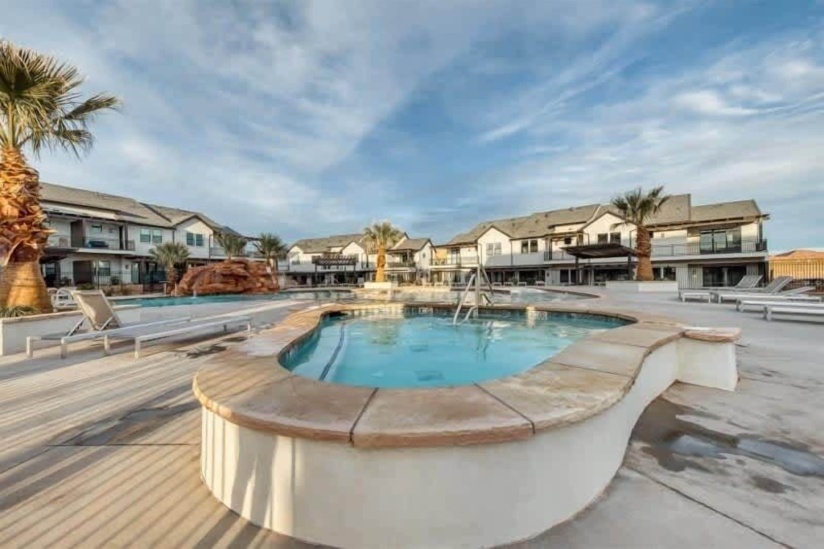 A swimming pool with a wooden deck, surrounded by modern buildings with balconies.
