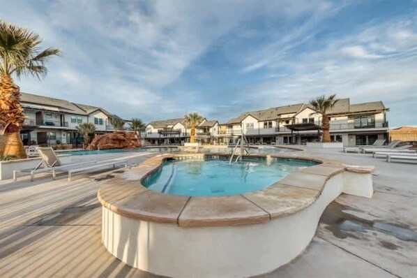 A swimming pool with a wooden deck, surrounded by modern buildings with balconies.