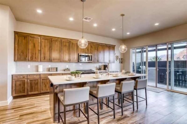 A modern kitchen with wooden cabinets, a central island with bar stools, and a large sliding glass door to the outdoors.