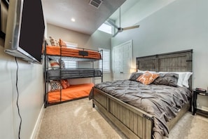 A bedroom with bunk beds, a large bed, a television, and a ceiling fan.