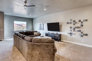 A living room with a sectional sofa, a flat-screen TV, and a wall with a word puzzle.