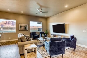 A living room with a sofa, armchairs, a coffee table, and a flat-screen TV mounted on the wall.