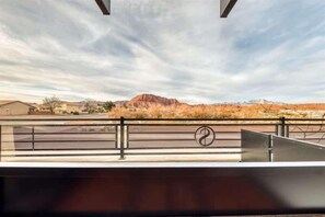 A view from a balcony with a metal railing, a mountain in the background, and a clear sky.